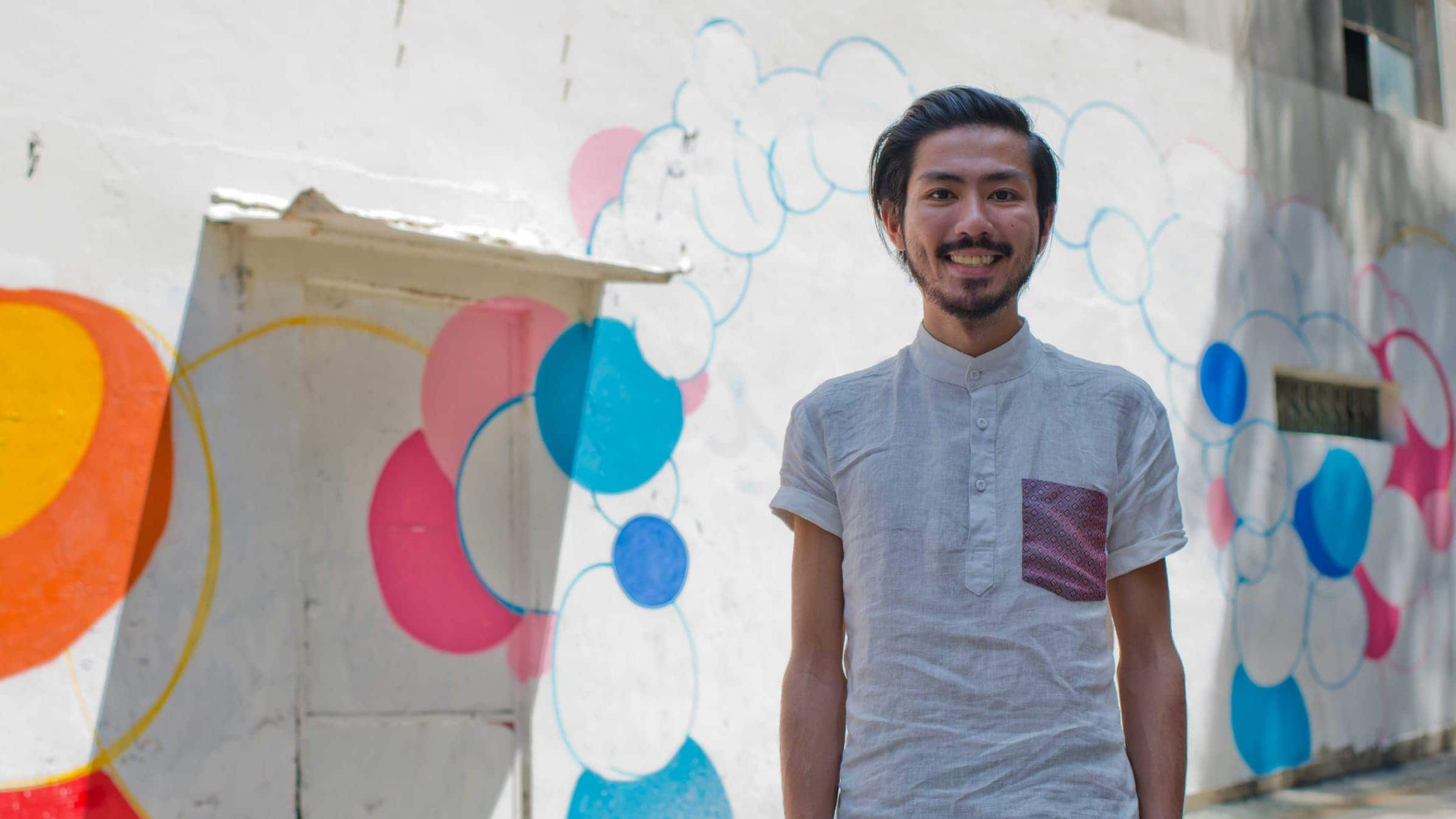 Jerome Tam, founder of Rush Hour Digital, stands in the street in front of a wall mural.